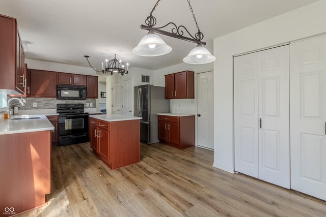 kitchen with a sink, light wood-style floors, black appliances, and a notable chandelier