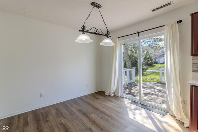 unfurnished dining area featuring baseboards, visible vents, and wood finished floors