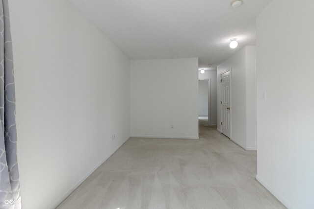 spare room with baseboards and light colored carpet