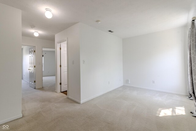 spare room with baseboards, light carpet, and visible vents