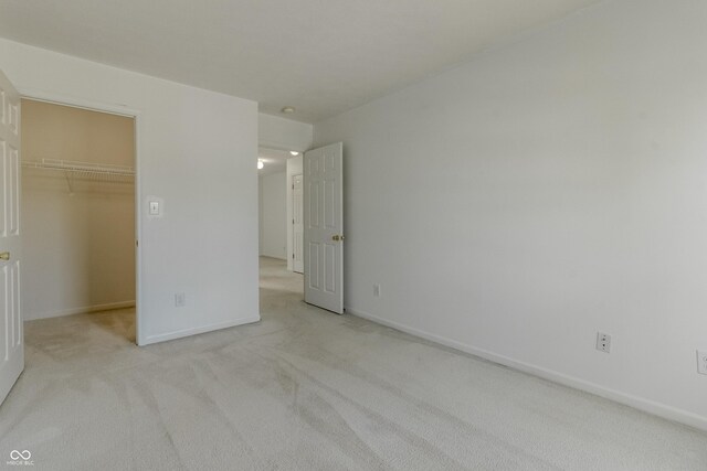 unfurnished bedroom featuring baseboards, light carpet, a closet, and a spacious closet