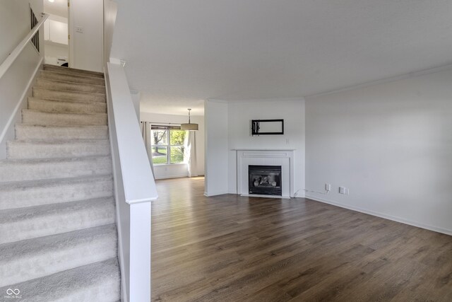 interior space featuring baseboards, a glass covered fireplace, ornamental molding, and wood finished floors