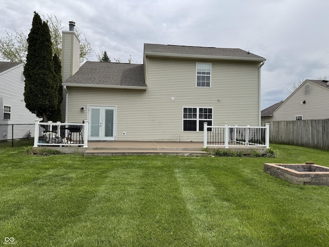 back of property with a lawn, a deck, an outdoor fire pit, french doors, and a fenced backyard