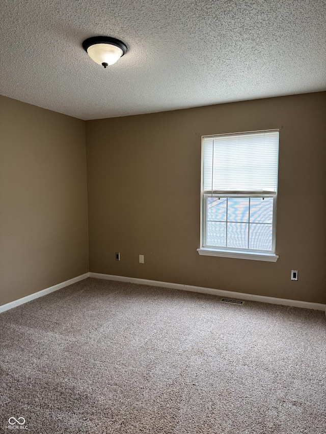 spare room featuring carpet, a textured ceiling, baseboards, and visible vents