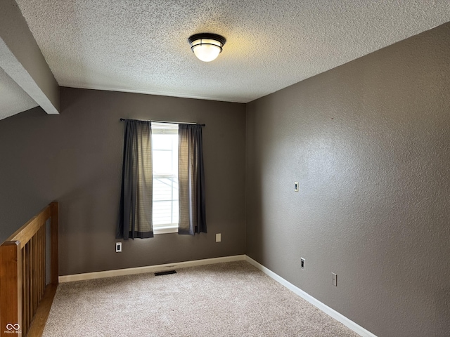 unfurnished room with carpet floors, a textured ceiling, baseboards, and visible vents