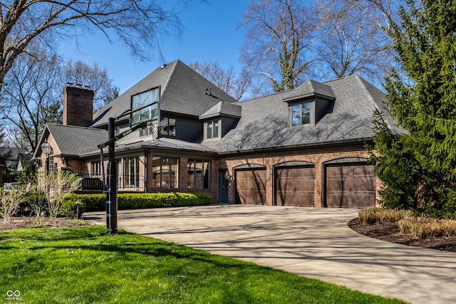view of front facade with concrete driveway, a chimney, roof with shingles, an attached garage, and brick siding