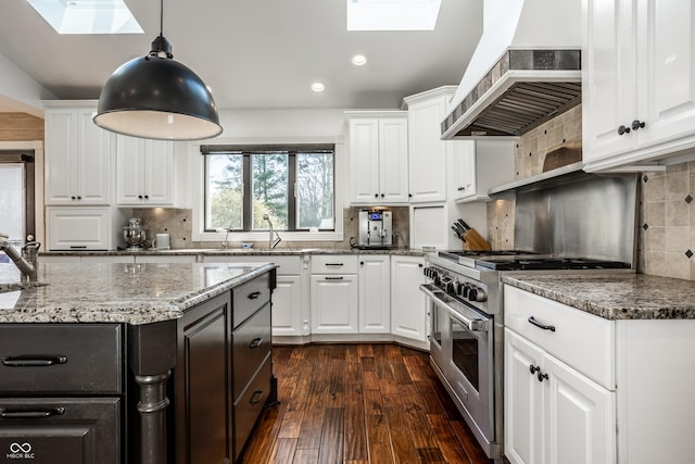 kitchen with a sink, a skylight, wall chimney exhaust hood, stainless steel stove, and backsplash