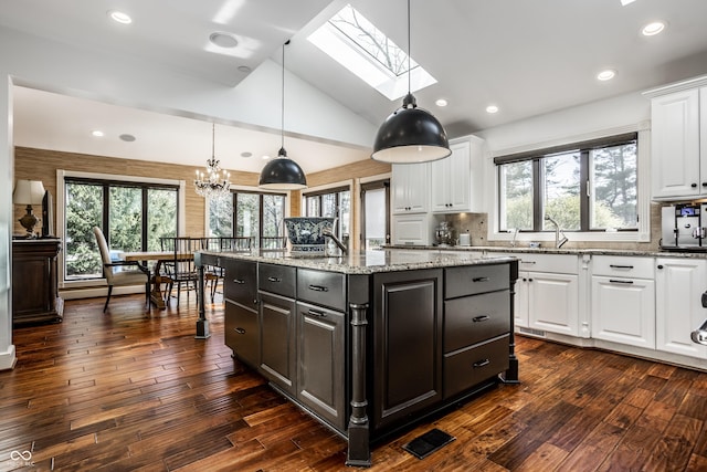 kitchen with vaulted ceiling with skylight, white cabinetry, an island with sink, and dark wood finished floors