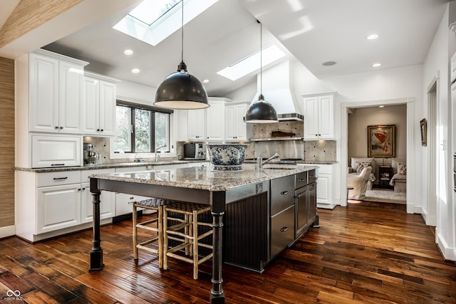 kitchen with tasteful backsplash, a center island with sink, white cabinetry, and dark wood finished floors
