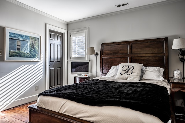 bedroom with wood finished floors, crown molding, visible vents, and baseboards