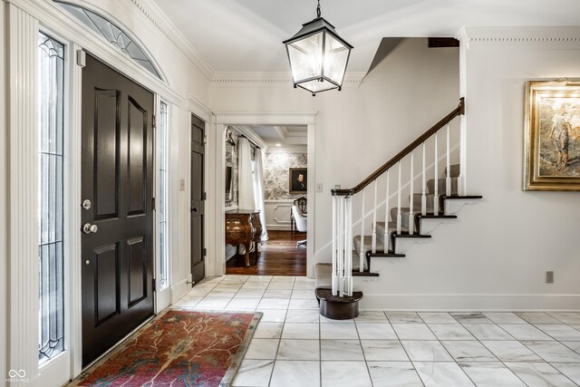 foyer entrance with crown molding, a chandelier, baseboards, marble finish floor, and stairs