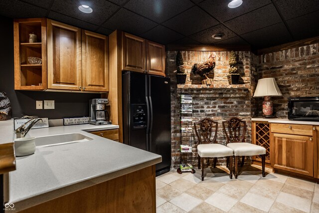 kitchen featuring a sink, brick wall, black refrigerator with ice dispenser, brown cabinetry, and light countertops