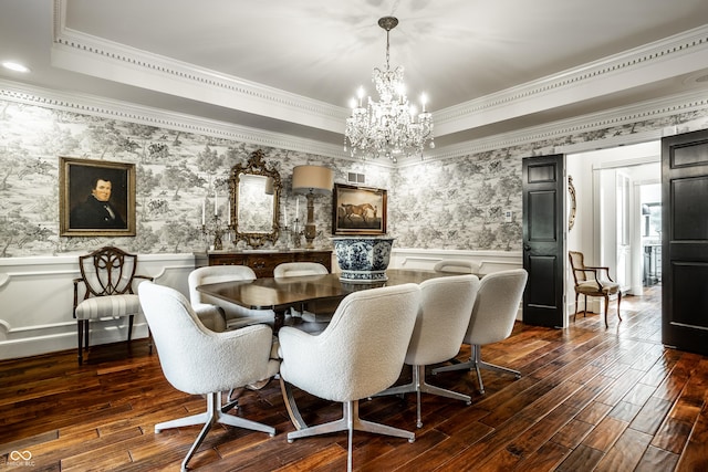 dining space featuring wainscoting, ornamental molding, dark wood-style flooring, a raised ceiling, and a notable chandelier