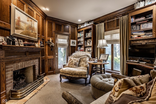 living area featuring a brick fireplace, crown molding, wooden walls, and carpet