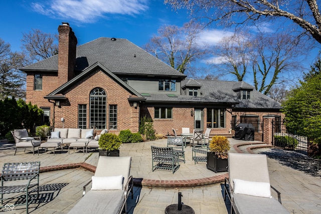 rear view of house featuring outdoor lounge area, brick siding, a patio area, and roof with shingles