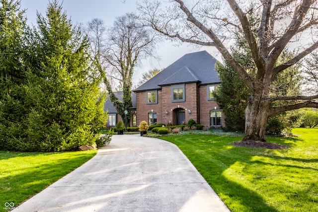 view of front of home featuring a front lawn, driveway, a shingled roof, and brick siding
