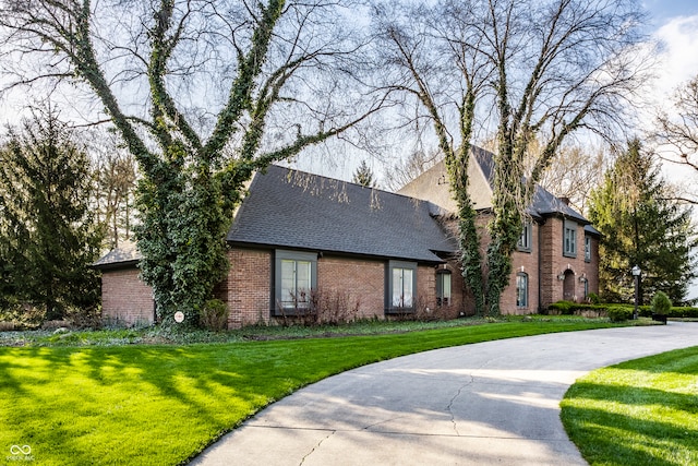 view of front of home with a front lawn, roof with shingles, and brick siding