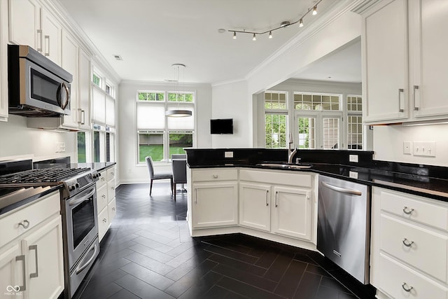 kitchen featuring appliances with stainless steel finishes, a sink, dark countertops, ornamental molding, and a peninsula
