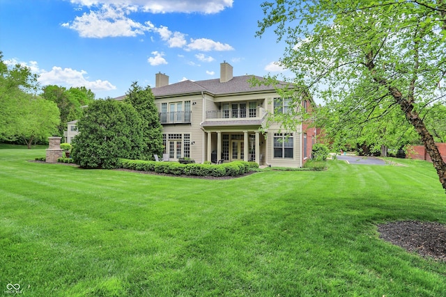 rear view of house with a lawn, a balcony, and a chimney