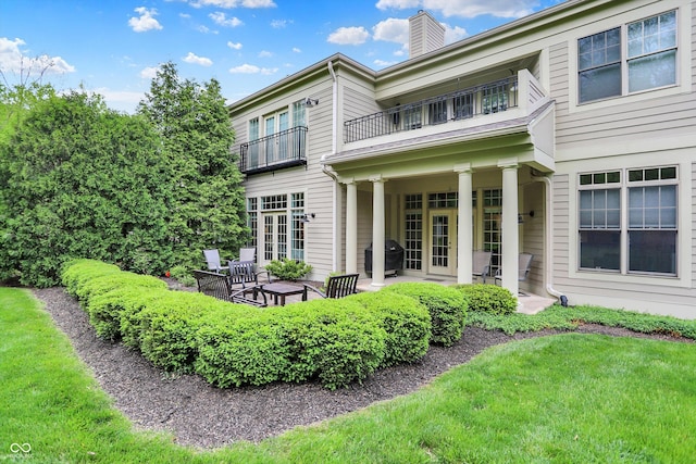 back of house featuring a balcony, a chimney, a patio area, and a lawn