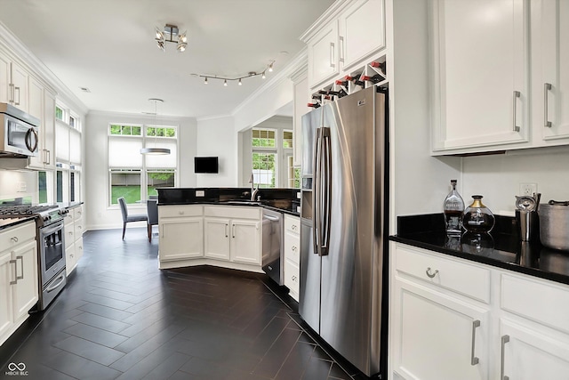 kitchen featuring appliances with stainless steel finishes, dark countertops, a peninsula, white cabinetry, and ornamental molding