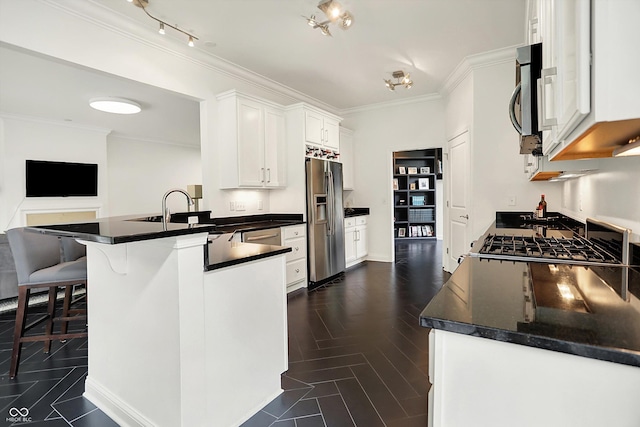 kitchen featuring appliances with stainless steel finishes, dark countertops, a peninsula, white cabinets, and ornamental molding