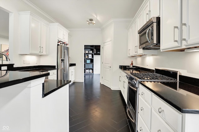 kitchen featuring appliances with stainless steel finishes, dark countertops, white cabinets, ornamental molding, and dark wood-style flooring