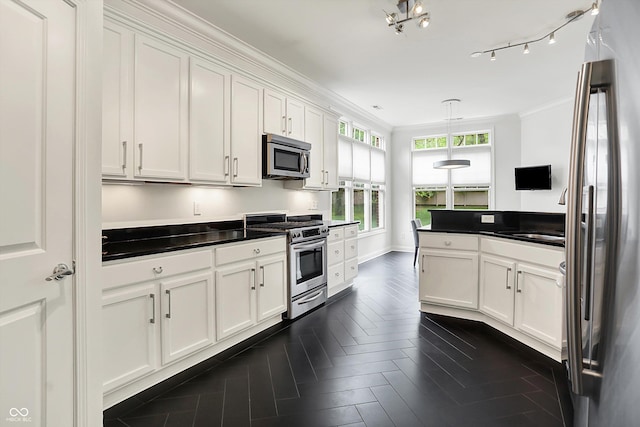 kitchen with appliances with stainless steel finishes, white cabinetry, dark countertops, ornamental molding, and decorative light fixtures