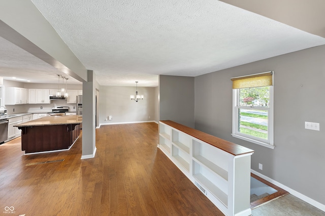 kitchen with open shelves, appliances with stainless steel finishes, an inviting chandelier, a textured ceiling, and a center island