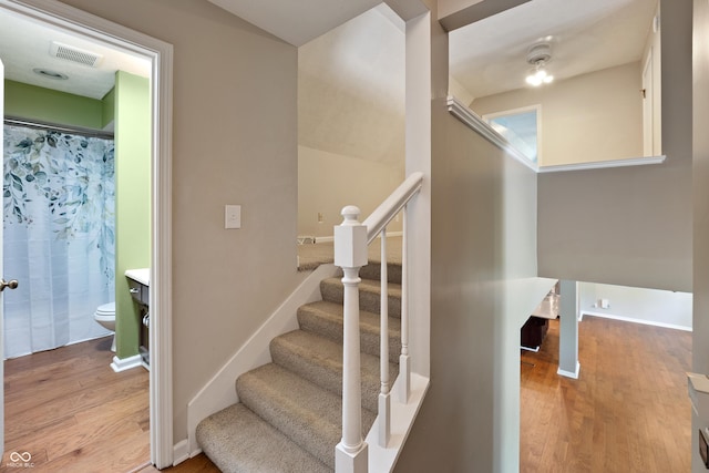 staircase with baseboards, visible vents, and wood finished floors