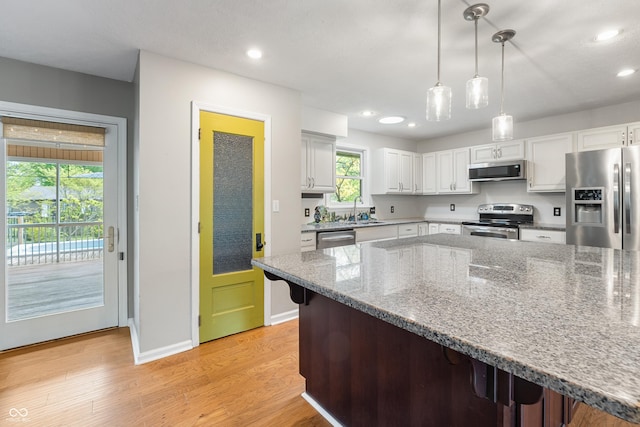 kitchen featuring white cabinets, a sink, a breakfast bar area, light wood-style flooring, and stainless steel appliances