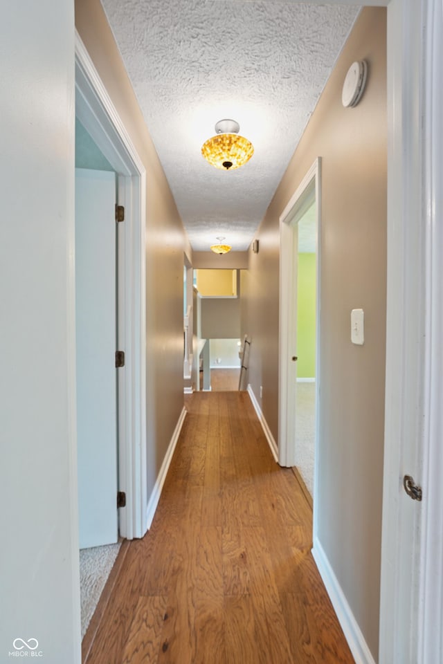 hall featuring baseboards, a textured ceiling, wood finished floors, and an upstairs landing