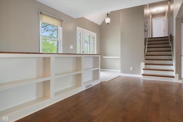 empty room featuring stairs, baseboards, wood finished floors, vaulted ceiling, and visible vents