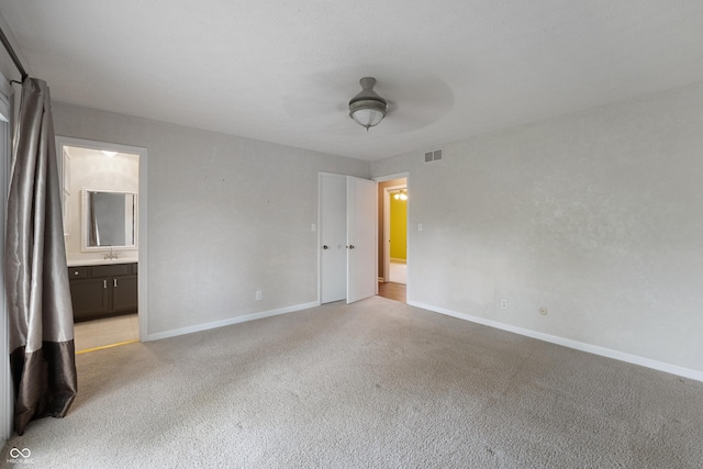 unfurnished bedroom featuring connected bathroom, light carpet, a sink, baseboards, and visible vents