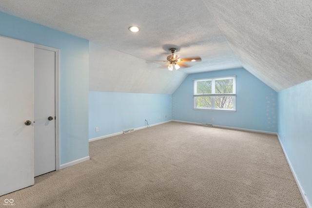 additional living space with a textured ceiling, visible vents, vaulted ceiling, baseboards, and carpet