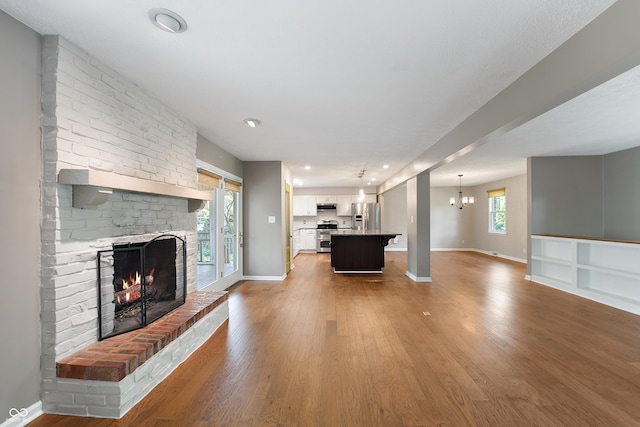 unfurnished living room with a brick fireplace, wood finished floors, baseboards, recessed lighting, and a notable chandelier