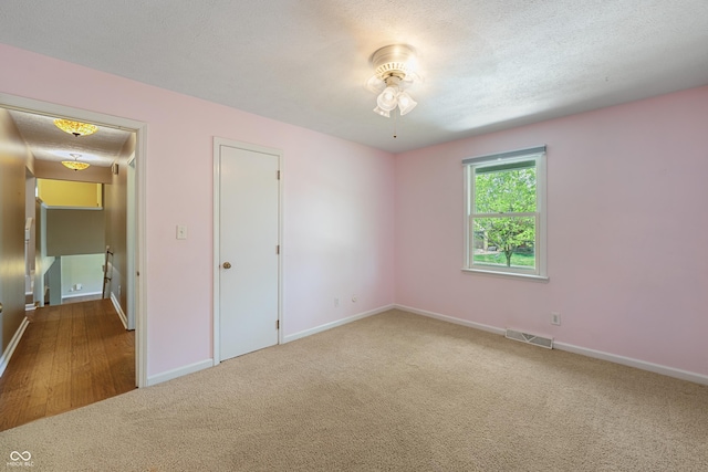 unfurnished bedroom featuring visible vents, a textured ceiling, carpet, and baseboards