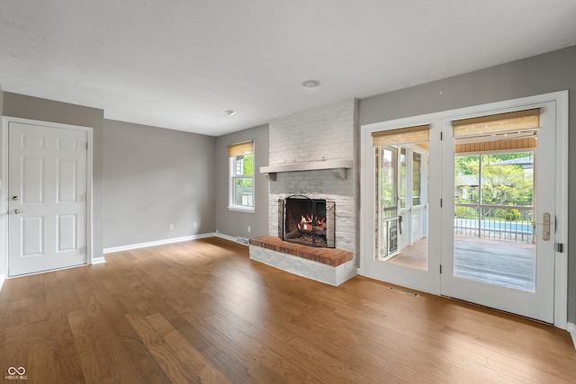unfurnished living room with visible vents, baseboards, a brick fireplace, and wood finished floors