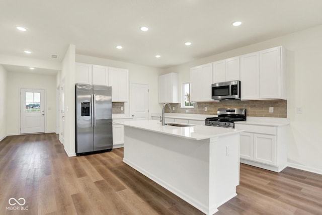 2712 Glade Ave, Plainfield, IN 46168 - kitchen with stainless steel appliances, a sink, decorative backsplash, white cabinetry, and a kitchen island with sink