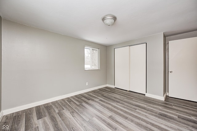 unfurnished bedroom featuring wood finished floors, a closet, and baseboards