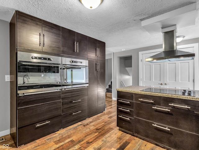 kitchen with stainless steel oven, black electric stovetop, island exhaust hood, and light wood-style floors