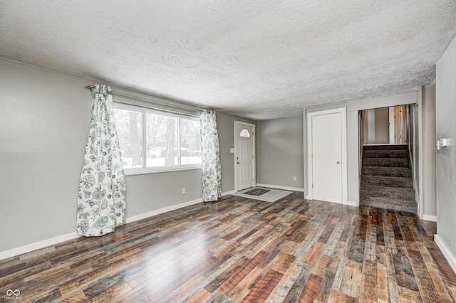 unfurnished living room with stairway, baseboards, wood finished floors, and a textured ceiling