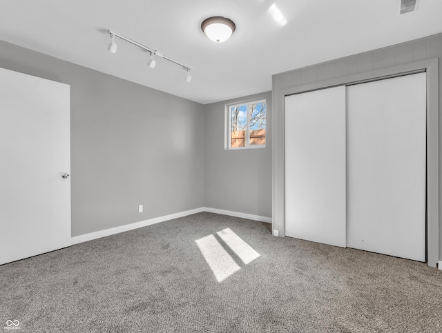 unfurnished bedroom with rail lighting, carpet floors, and a closet