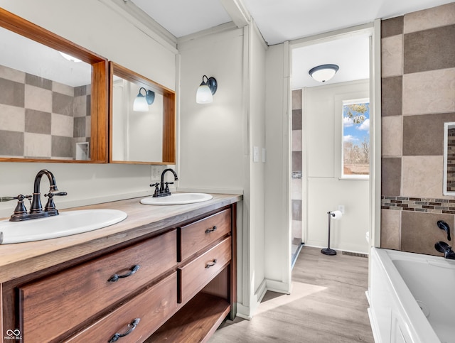 bathroom featuring a bathtub, double vanity, wood finished floors, and a sink