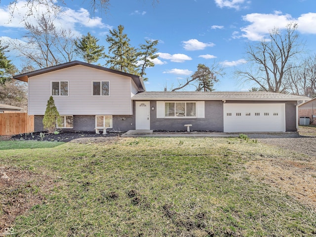 split level home with a front lawn, driveway, fence, brick siding, and an attached garage