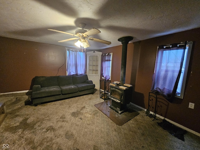 living area featuring a ceiling fan, a textured ceiling, a wood stove, baseboards, and carpet flooring