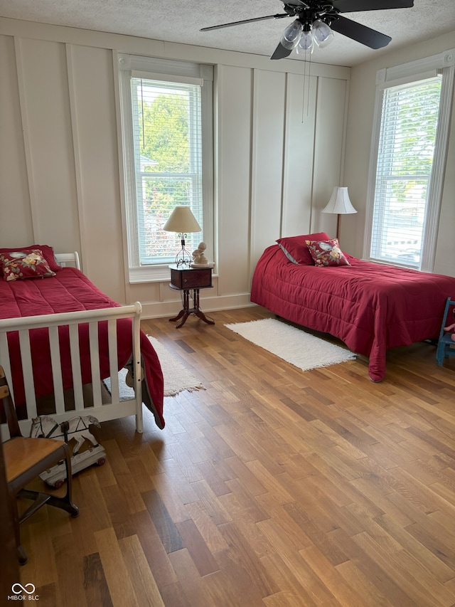 bedroom with a textured ceiling, wood finished floors, a decorative wall, and multiple windows
