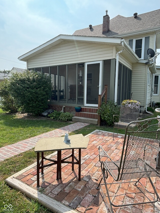 rear view of property featuring a chimney, a yard, roof with shingles, a patio, and a sunroom