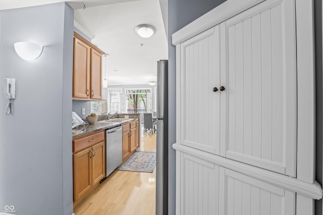 kitchen featuring stainless steel dishwasher, brown cabinets, a sink, and light wood-style flooring