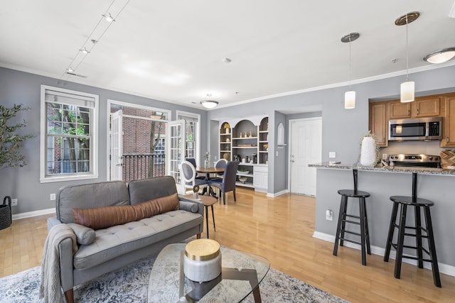 living area featuring baseboards, ornamental molding, light wood-style flooring, and built in shelves
